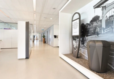 Moderne, lichte kantoorruimte aan de Barbara Strozzilaan met een kunstinstallatie van een afvalbak en informatiebord voor een muurfoto van een historisch straatbeeld.